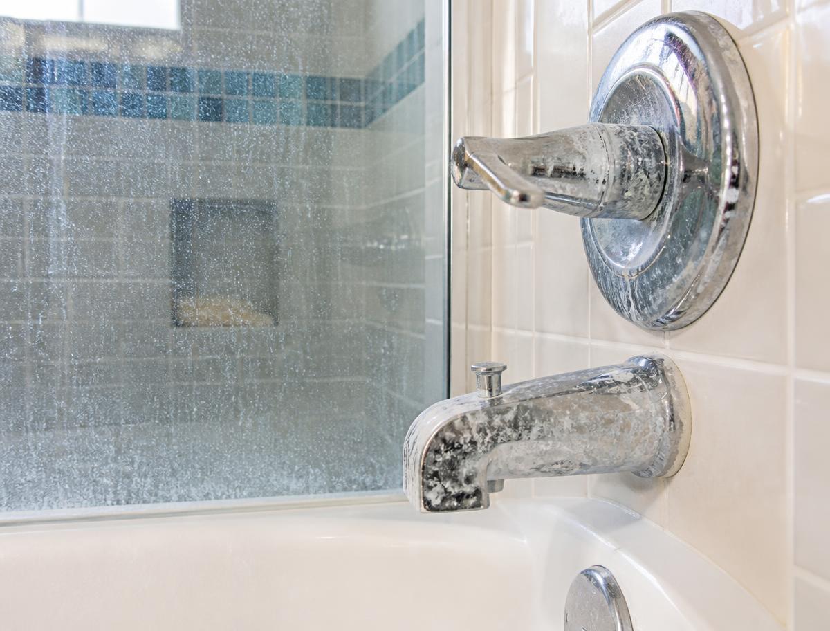 Visible white mineral scale on a bathtub faucet and shower glass
